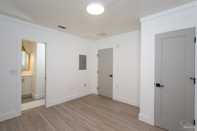 unfurnished bedroom featuring visible vents, electric panel, ensuite bath, light wood finished floors, and baseboards