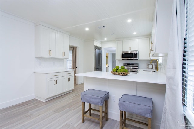 kitchen with a breakfast bar area, light wood-style flooring, a sink, stainless steel appliances, and white cabinets