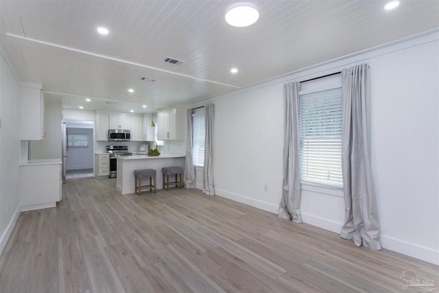 interior space with light wood-type flooring, appliances with stainless steel finishes, kitchen peninsula, and white cabinetry