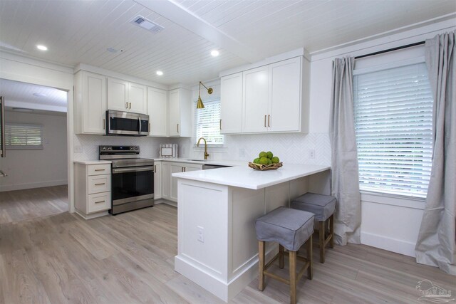 kitchen with plenty of natural light, kitchen peninsula, a breakfast bar, and appliances with stainless steel finishes