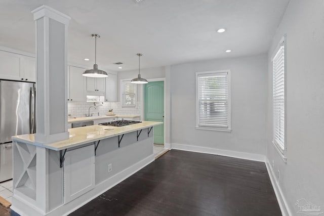 kitchen with appliances with stainless steel finishes, backsplash, white cabinets, a kitchen island, and decorative light fixtures