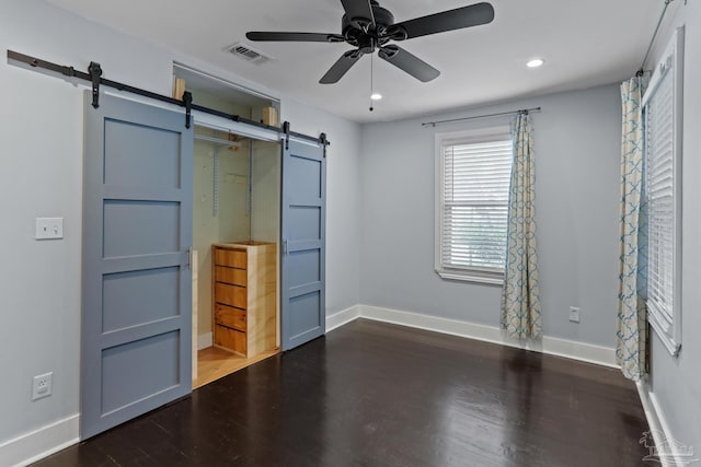 unfurnished bedroom featuring a barn door, dark wood-type flooring, and ceiling fan