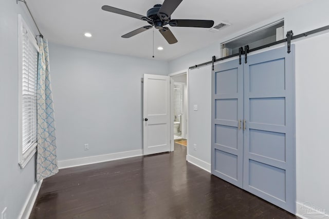 unfurnished bedroom featuring a barn door, dark wood-type flooring, and ceiling fan