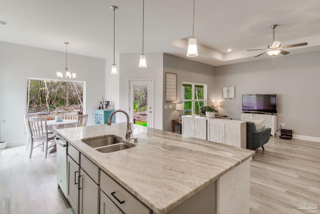 kitchen featuring light wood-type flooring, an island with sink, a sink, stainless steel dishwasher, and light stone countertops