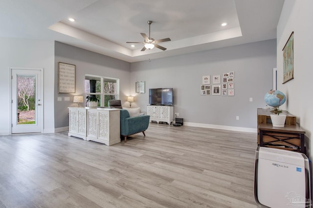 living room with a raised ceiling, a ceiling fan, baseboards, and light wood finished floors