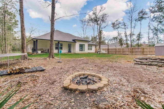 back of house featuring a trampoline, an outdoor fire pit, and fence