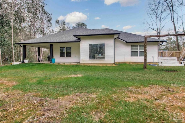 rear view of property with a shingled roof, a yard, and fence