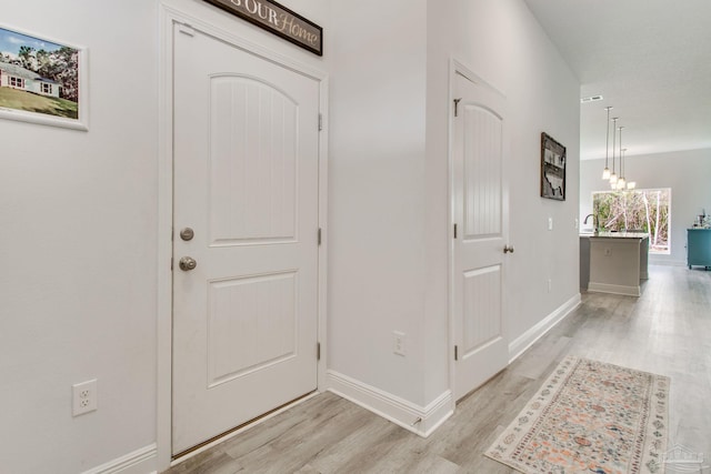 hallway with light wood-type flooring, baseboards, and a notable chandelier