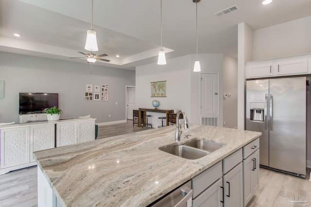 kitchen with visible vents, a sink, a tray ceiling, light wood-style floors, and appliances with stainless steel finishes