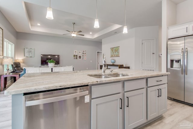 kitchen with a ceiling fan, a sink, a tray ceiling, open floor plan, and appliances with stainless steel finishes