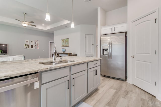 kitchen featuring light wood finished floors, light stone countertops, appliances with stainless steel finishes, a raised ceiling, and a ceiling fan