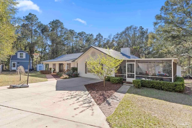 ranch-style home with a chimney, concrete driveway, a front lawn, and a sunroom