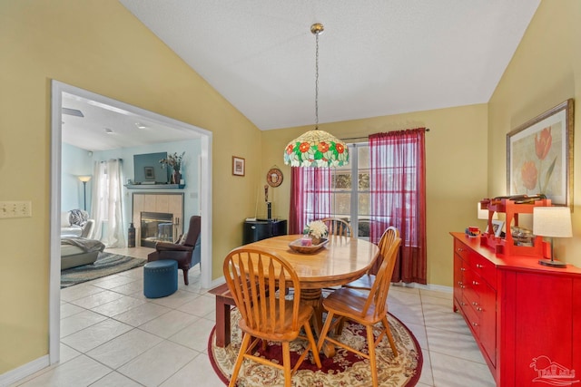 dining area featuring light tile patterned floors, baseboards, lofted ceiling, and a tiled fireplace