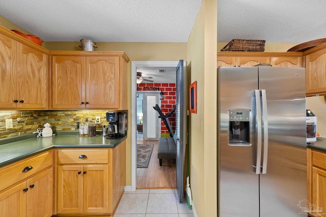 kitchen featuring dark countertops, stainless steel fridge with ice dispenser, light tile patterned floors, decorative backsplash, and a textured ceiling