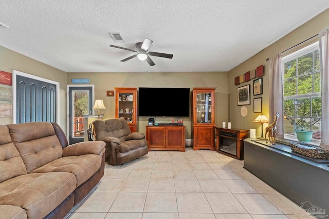 living area featuring light tile patterned floors, visible vents, a textured ceiling, and a ceiling fan