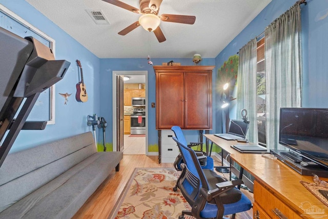 office area with a ceiling fan, light wood-style floors, visible vents, and a textured ceiling