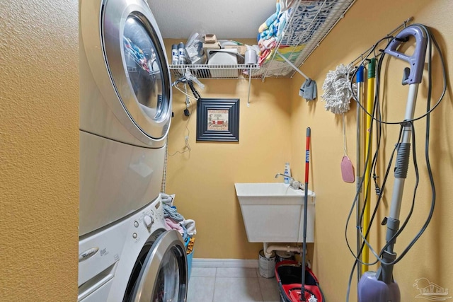 clothes washing area featuring tile patterned flooring, laundry area, baseboards, and stacked washer and dryer