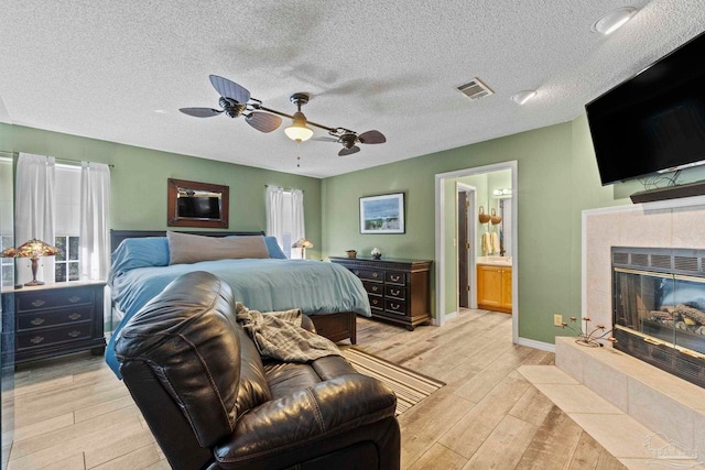 bedroom featuring visible vents, ensuite bath, light wood-style flooring, a tile fireplace, and a textured ceiling