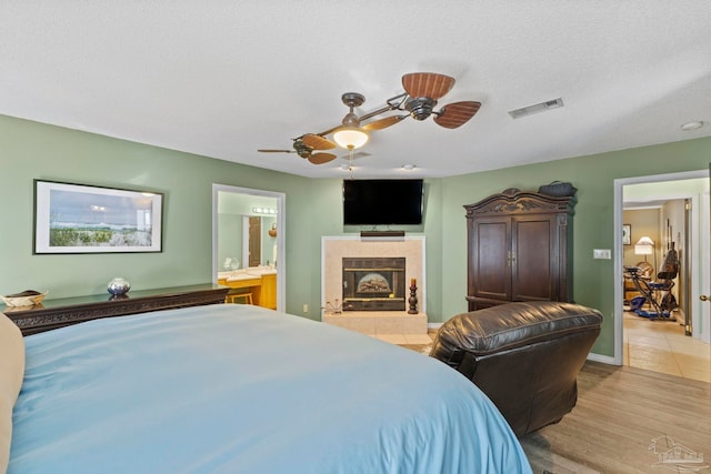 bedroom with light wood finished floors, visible vents, a fireplace, ensuite bathroom, and a textured ceiling