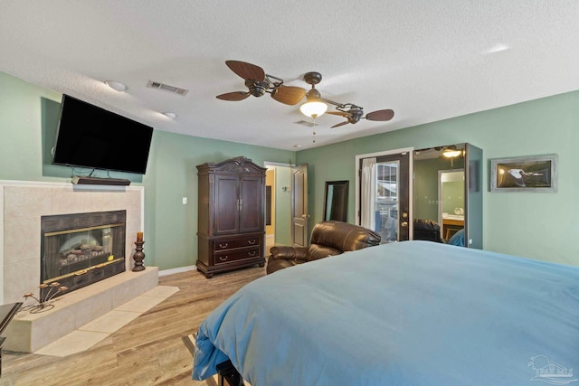 bedroom featuring visible vents, a textured ceiling, light wood-style flooring, and a tiled fireplace