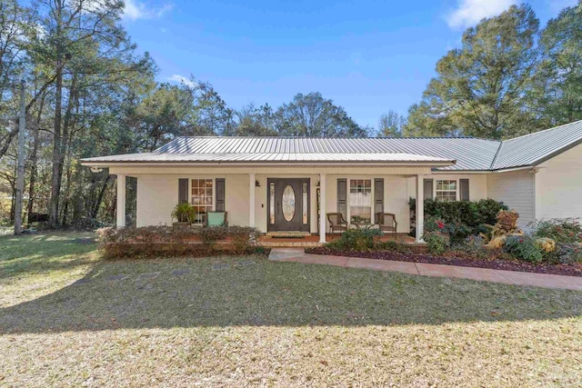 ranch-style home featuring covered porch, metal roof, a front lawn, and stucco siding