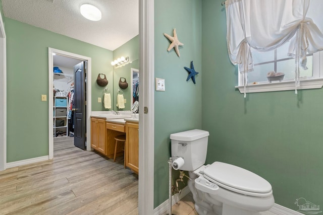 bathroom featuring baseboards, toilet, vanity, wood finished floors, and a textured ceiling