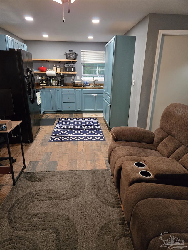 kitchen with light wood-type flooring, blue cabinetry, a sink, black fridge with ice dispenser, and open floor plan