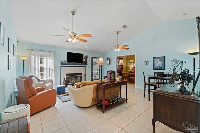 living area with visible vents, a ceiling fan, light tile patterned floors, lofted ceiling, and a tile fireplace