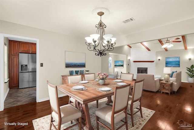 dining space with a fireplace, ceiling fan with notable chandelier, dark wood-type flooring, and beamed ceiling