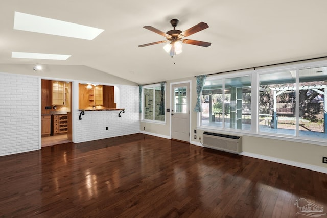 unfurnished living room with a wall mounted air conditioner, vaulted ceiling with skylight, brick wall, ceiling fan, and dark wood-type flooring