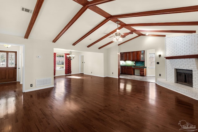 unfurnished living room featuring dark hardwood / wood-style flooring, a fireplace, lofted ceiling with beams, and ceiling fan with notable chandelier