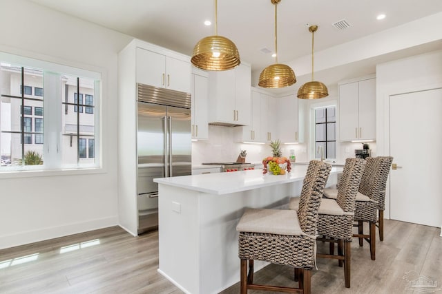 kitchen with visible vents, a breakfast bar, light wood-style flooring, light countertops, and built in fridge