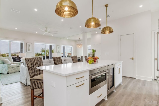 kitchen featuring open floor plan, wine cooler, light wood-style floors, a breakfast bar area, and stainless steel oven