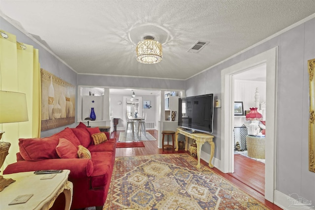 living room with a textured ceiling, wood finished floors, visible vents, and crown molding