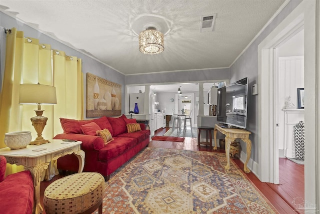 living room with crown molding, visible vents, a textured ceiling, ornate columns, and hardwood / wood-style flooring