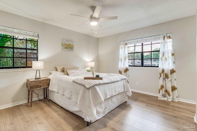 bedroom with ceiling fan, a textured ceiling, multiple windows, and light hardwood / wood-style floors