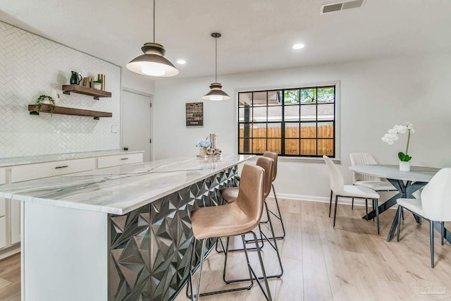 kitchen with decorative backsplash, light hardwood / wood-style flooring, decorative light fixtures, white cabinets, and light stone counters