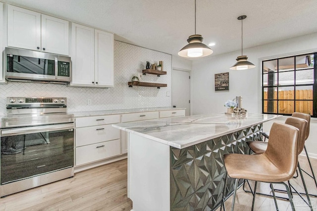 kitchen with appliances with stainless steel finishes, a center island, white cabinets, light stone counters, and light hardwood / wood-style flooring