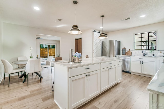 kitchen with hanging light fixtures, light stone countertops, a center island, white cabinetry, and appliances with stainless steel finishes