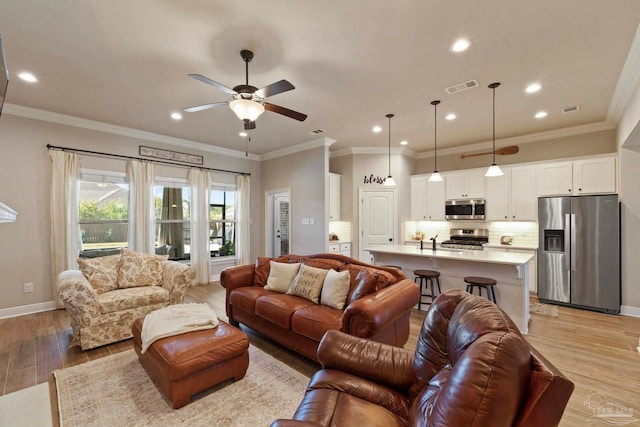 living room featuring ceiling fan, ornamental molding, and light wood-type flooring