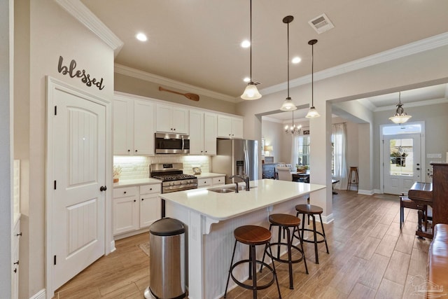 kitchen with light hardwood / wood-style floors, appliances with stainless steel finishes, a center island with sink, and hanging light fixtures