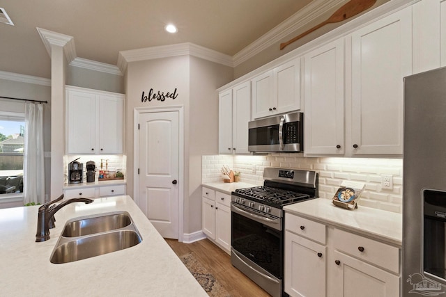 kitchen featuring hardwood / wood-style flooring, stainless steel appliances, ornamental molding, sink, and white cabinetry