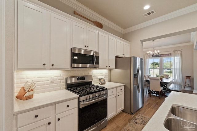 kitchen with hardwood / wood-style flooring, stainless steel appliances, crown molding, decorative light fixtures, and white cabinetry