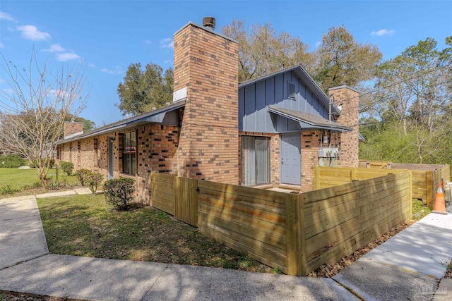 view of front of house with a fenced front yard, brick siding, board and batten siding, and a chimney