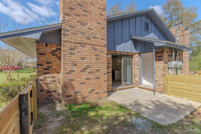 rear view of house featuring brick siding, board and batten siding, fence, a chimney, and a patio