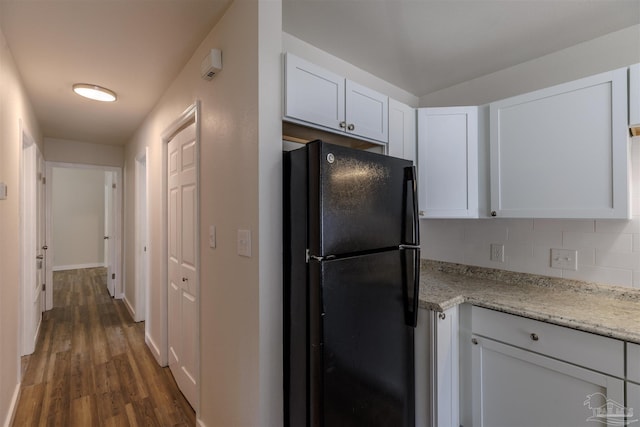 kitchen with backsplash, light stone counters, freestanding refrigerator, wood finished floors, and white cabinets