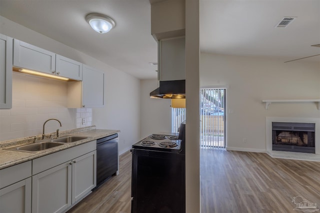 kitchen featuring under cabinet range hood, dishwashing machine, light wood-style flooring, decorative backsplash, and a sink