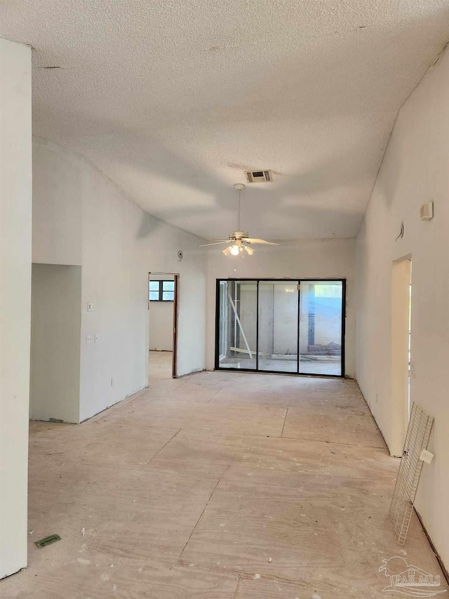 unfurnished room featuring vaulted ceiling, a healthy amount of sunlight, a textured ceiling, and ceiling fan