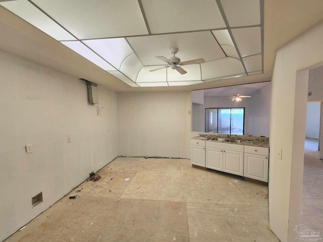 interior space with a ceiling fan, a raised ceiling, white cabinets, and a sink