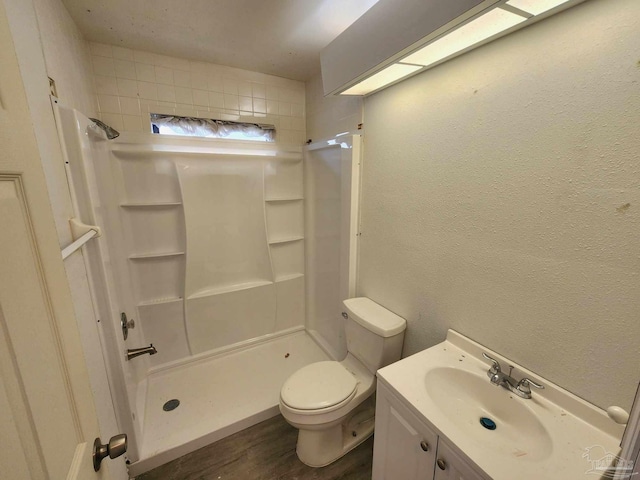 full bathroom with a stall shower, a textured wall, toilet, wood finished floors, and vanity